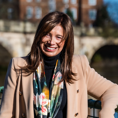Woman with brown hair with river and bridge in background.