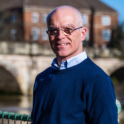 Man wearing glasses navy blue jumper with river and bridge in background