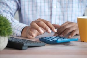 a person using a blue calculator on a desk with yellow cup