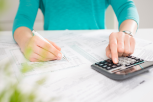 Woman wearing turqoise jumper using a calculator and checking figures