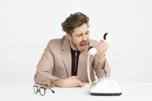 Man shouting frustratingly into a traditional telephone