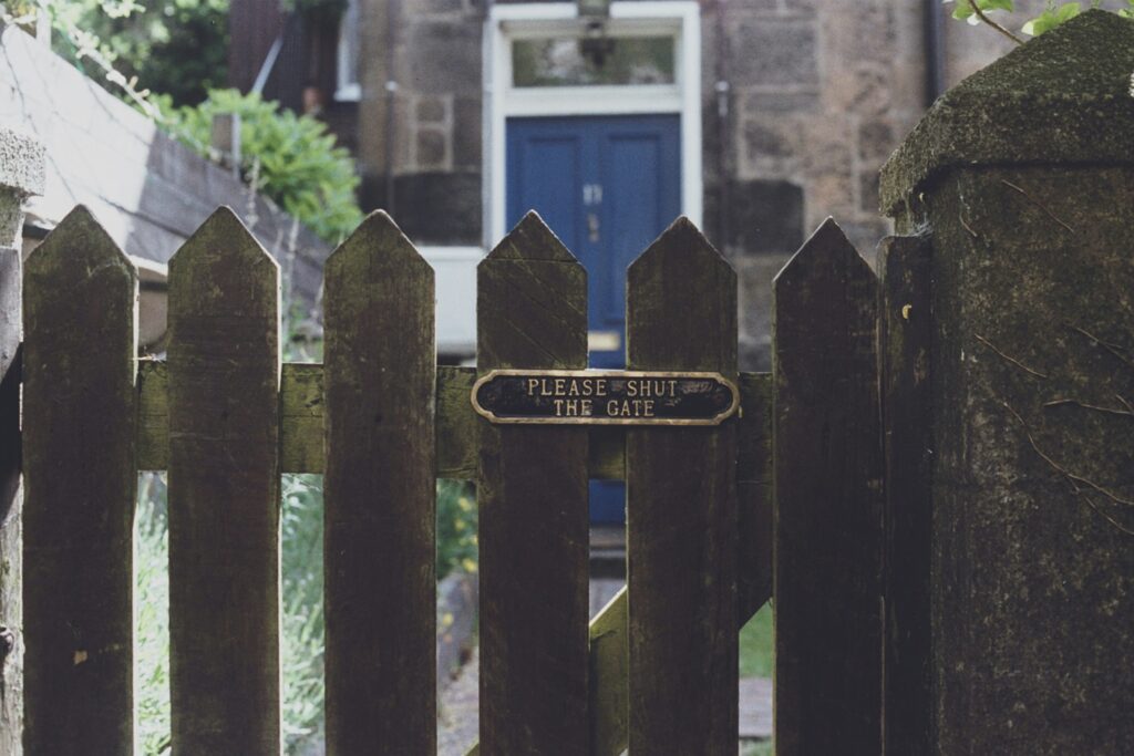 Wooden gate with brass sign showing please shut the gate - front door in blue