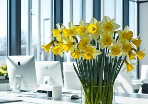 Bunch of daffodils on a desk with computer monitors behind