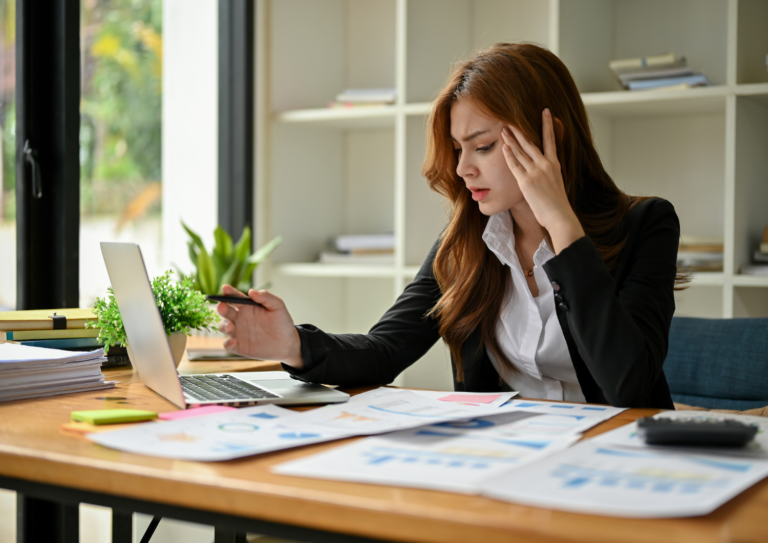 Woman in an office with papers on desk looking thoughtful