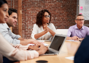 Men and women sitting around a table in an office setting, listening to one another and smiling