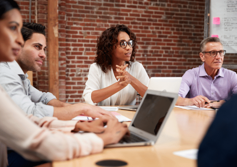 Men and women sitting around a table in an office setting, listening to one another and smiling