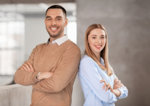 Two people in an office setting with arms folded back to back smiling as if alies