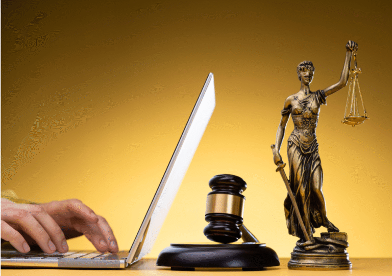 scales of justice figurine a gavel and a person on a laptop typing set against a yellow backdrop