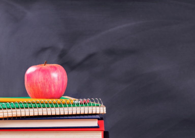 A picture of a rosy red apple on top of a stack of brightly coloured books set against the backdrop of a chalk board - to depict learning