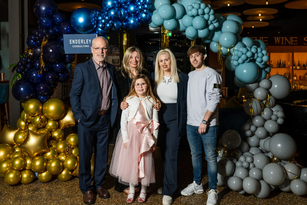 The Austin family smiling into the camera under a balloon arch at a party