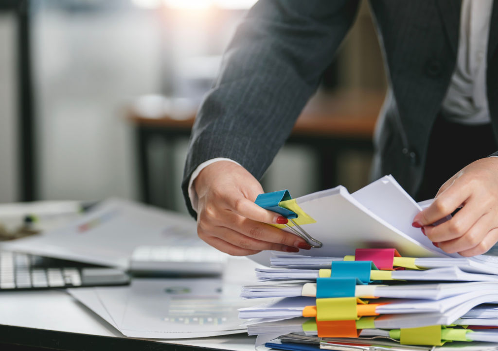 A person handling piles of paperwork on a desk grouped together with brightly coloured clips