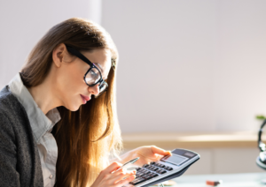 A woman in business attire and office setting working on a calculator